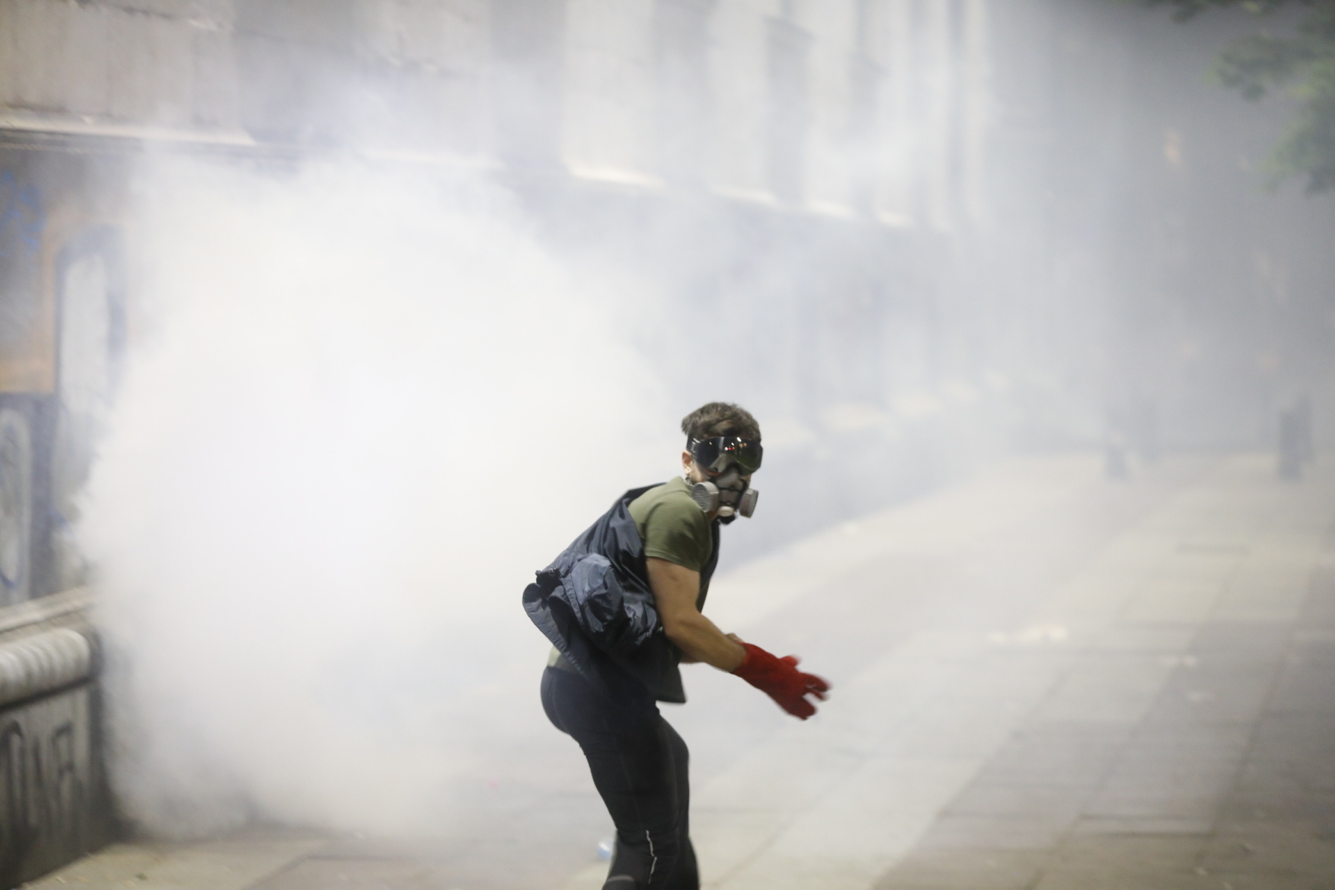 A protester wearing a gas mask runs through the streets of Tbilisi surrounded by tear gas.