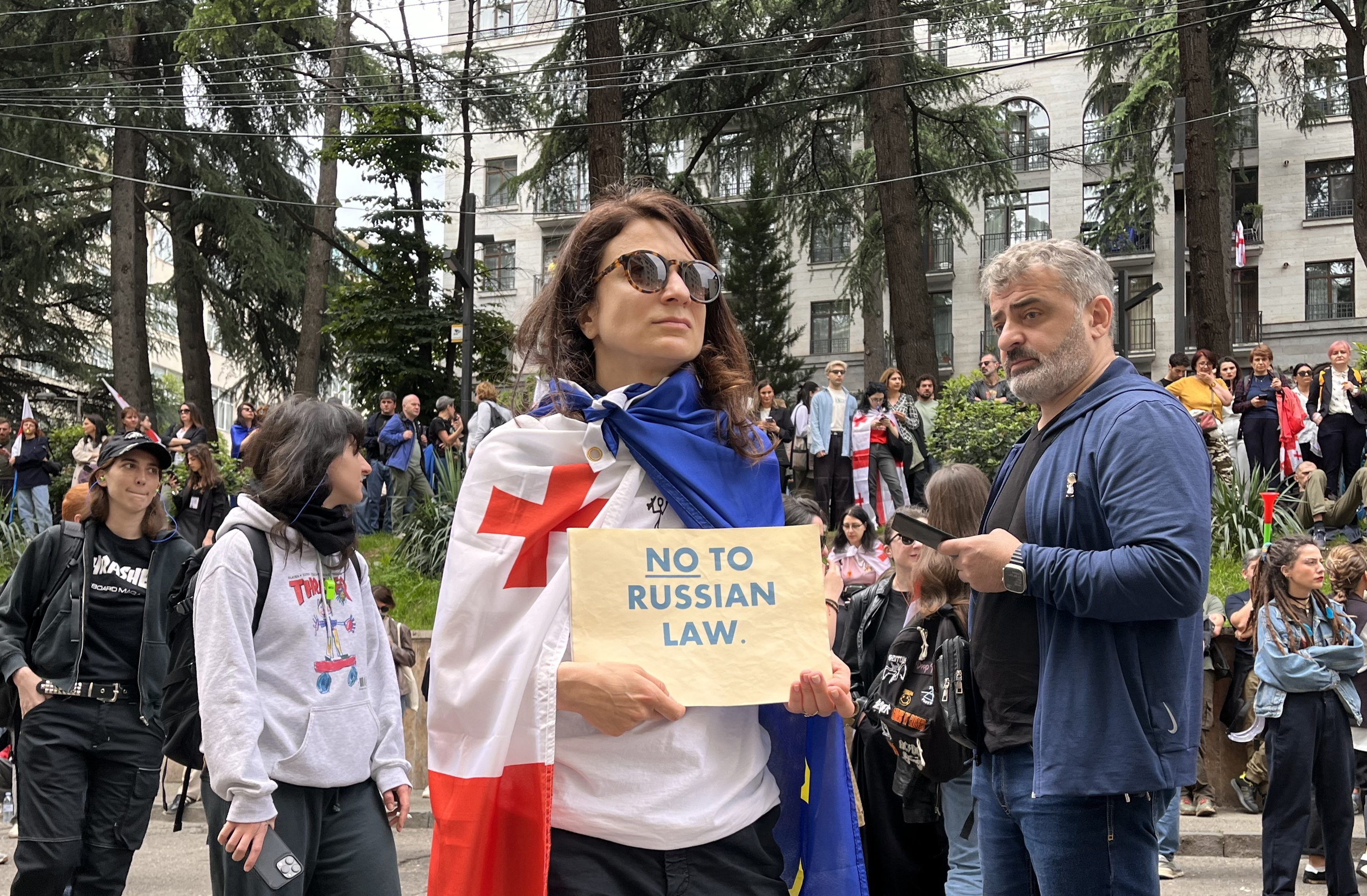 A woman in the middle of a demonstration has tied a Georgian flag over her shoulders and is holding a sign that reads "No to Russian law"