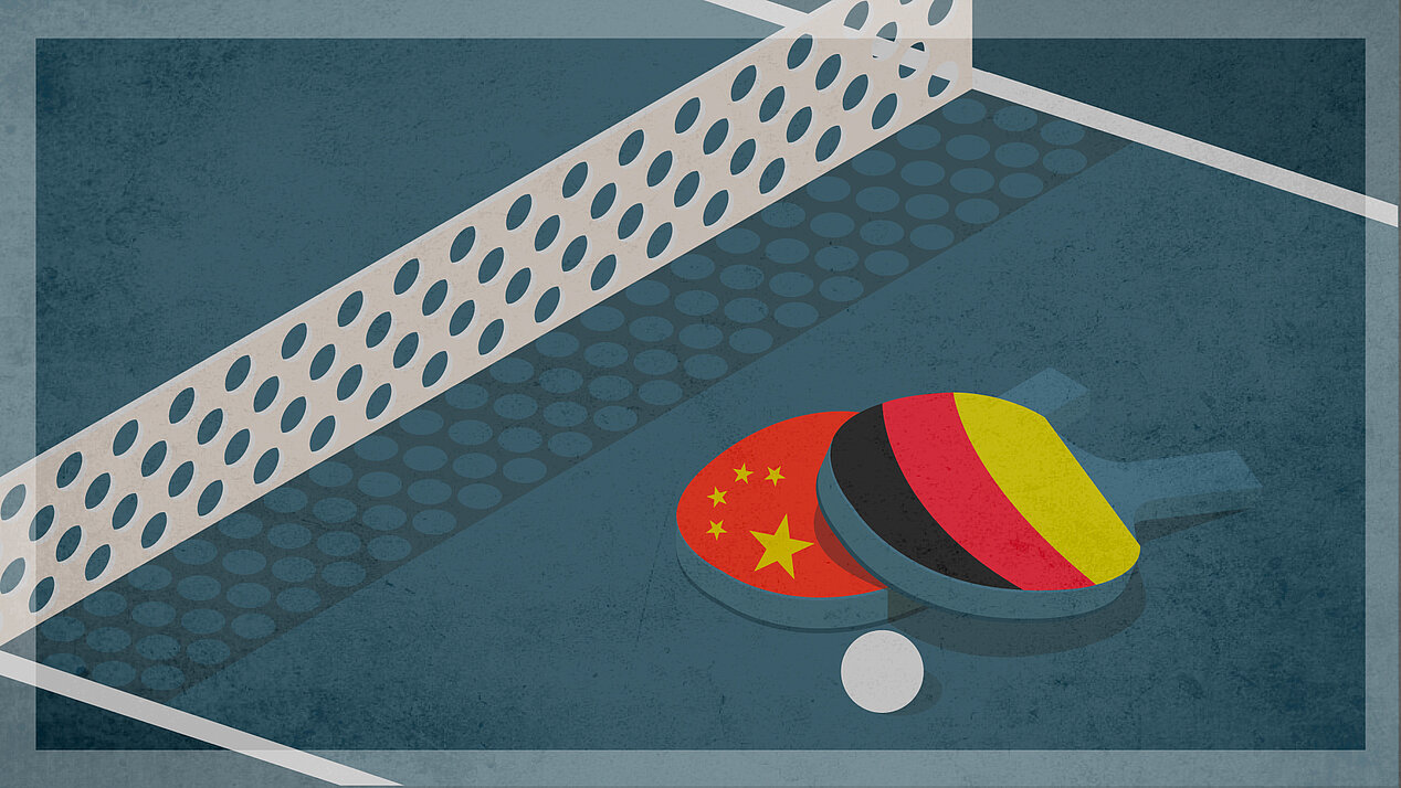 Tischtennisplatte mit zwei Tischtennisschlägern auf denen jeweils die chinesische und die deutsche Flagge abgebildet ist.