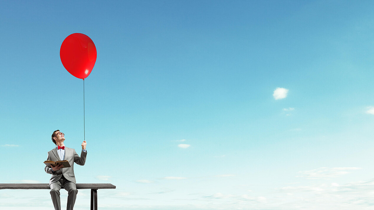 Illustration: A businessman is sitting on a bench in the sky. In one hand he holds an open book, in the other a red balloon.